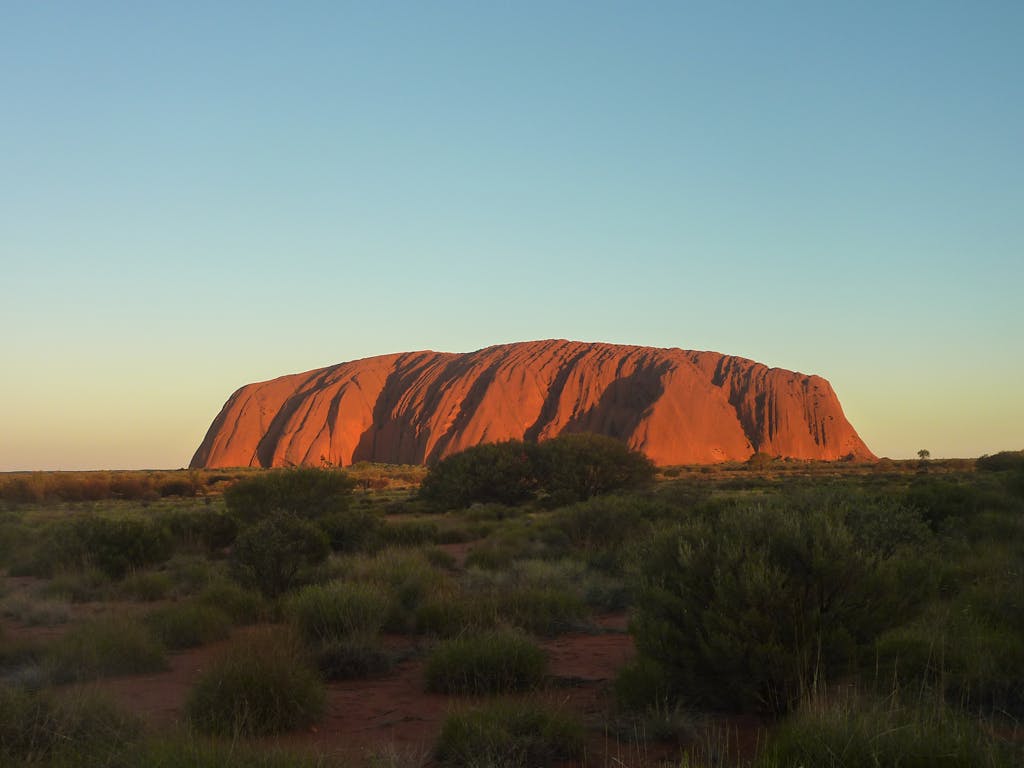 Capture the majestic Uluru rock formation glowing under the sunset. A natural wonder in Australia's Outback.