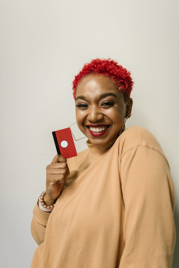 Vibrant portrait of a woman with short red hair holding a red card, smiling indoors.